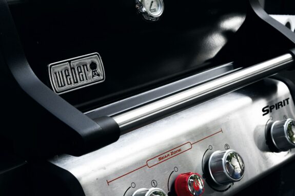 A closed stainless steel Weber gas grill sitting outdoors in a backyard garden setting