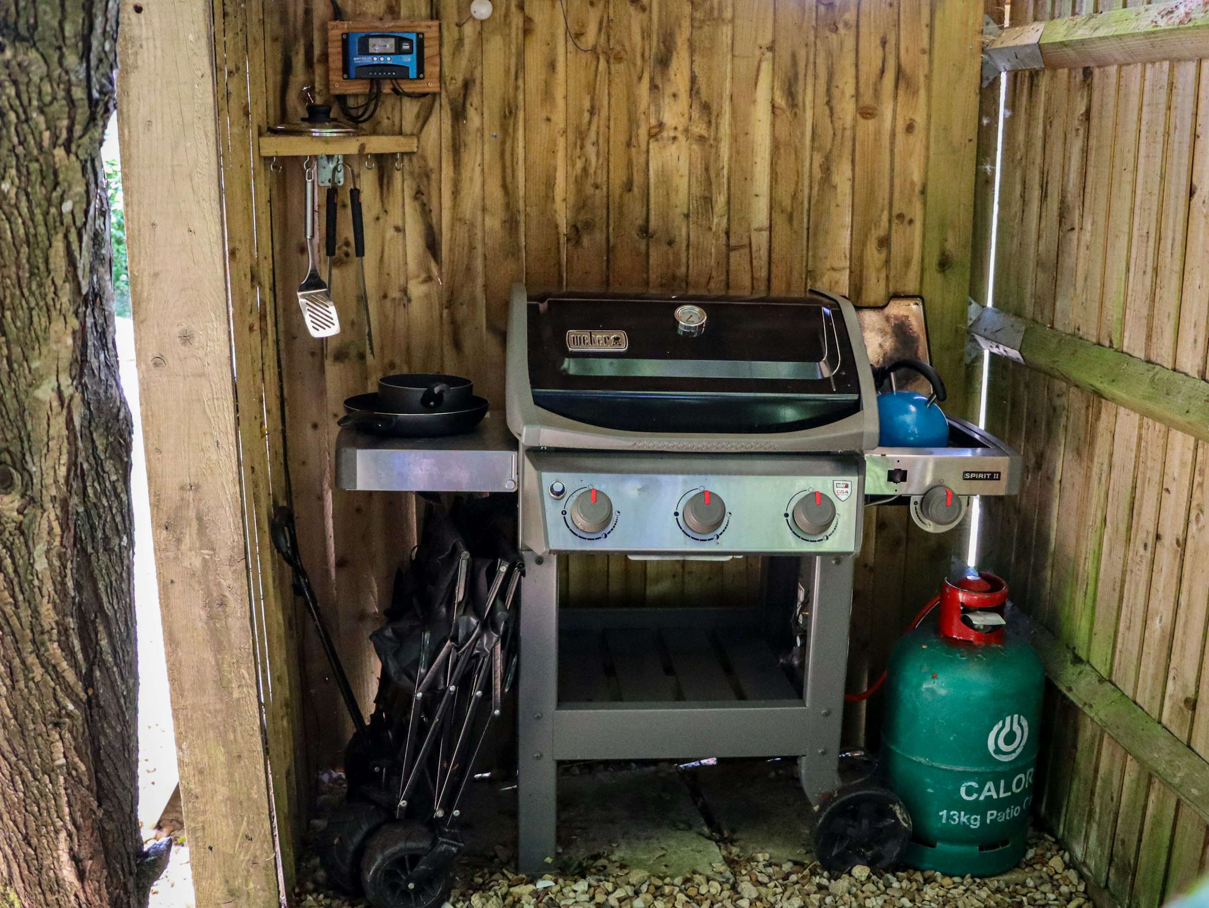 A gas grill with an attached propane tank set inside a wooden outdoor shelter.