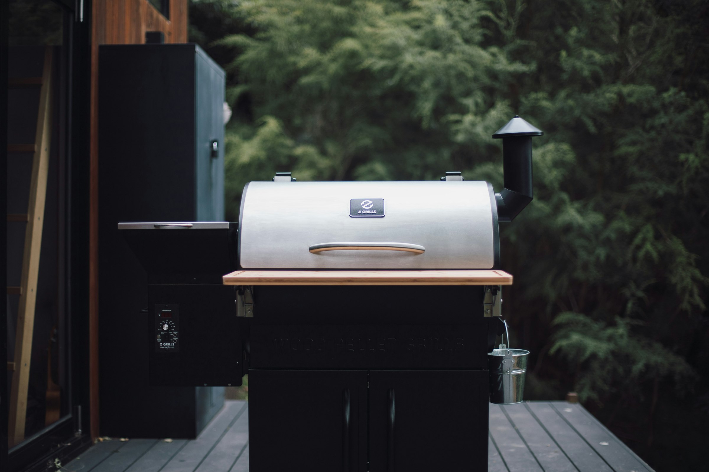A black and silver outdoor pellet grill sitting on a backyard patio surrounded by lawn and landscaping.
