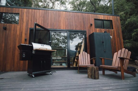 A black gas grill positioned outdoors on a patio beside a wooden wall