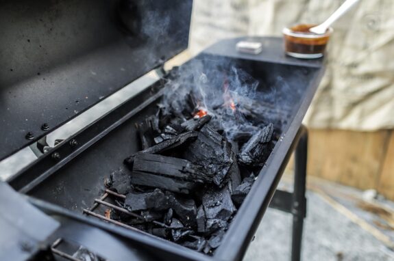 Open charcoal grill firebox filled with burning charcoal briquettes, glowing embers, and rising smoke