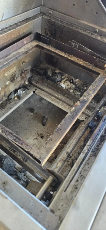 Grill firebox with grates removed showing grease and debris buildup before cleaning
